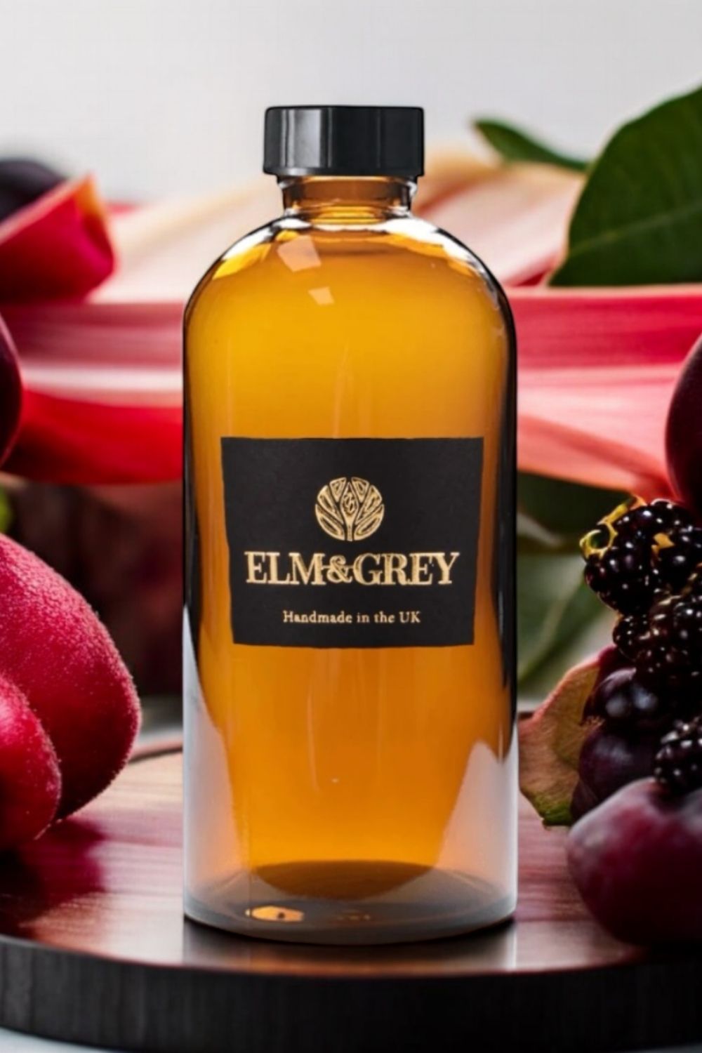 Bottle of Elm & Grey diffuser refill surrounded by fruits on a wooden surface