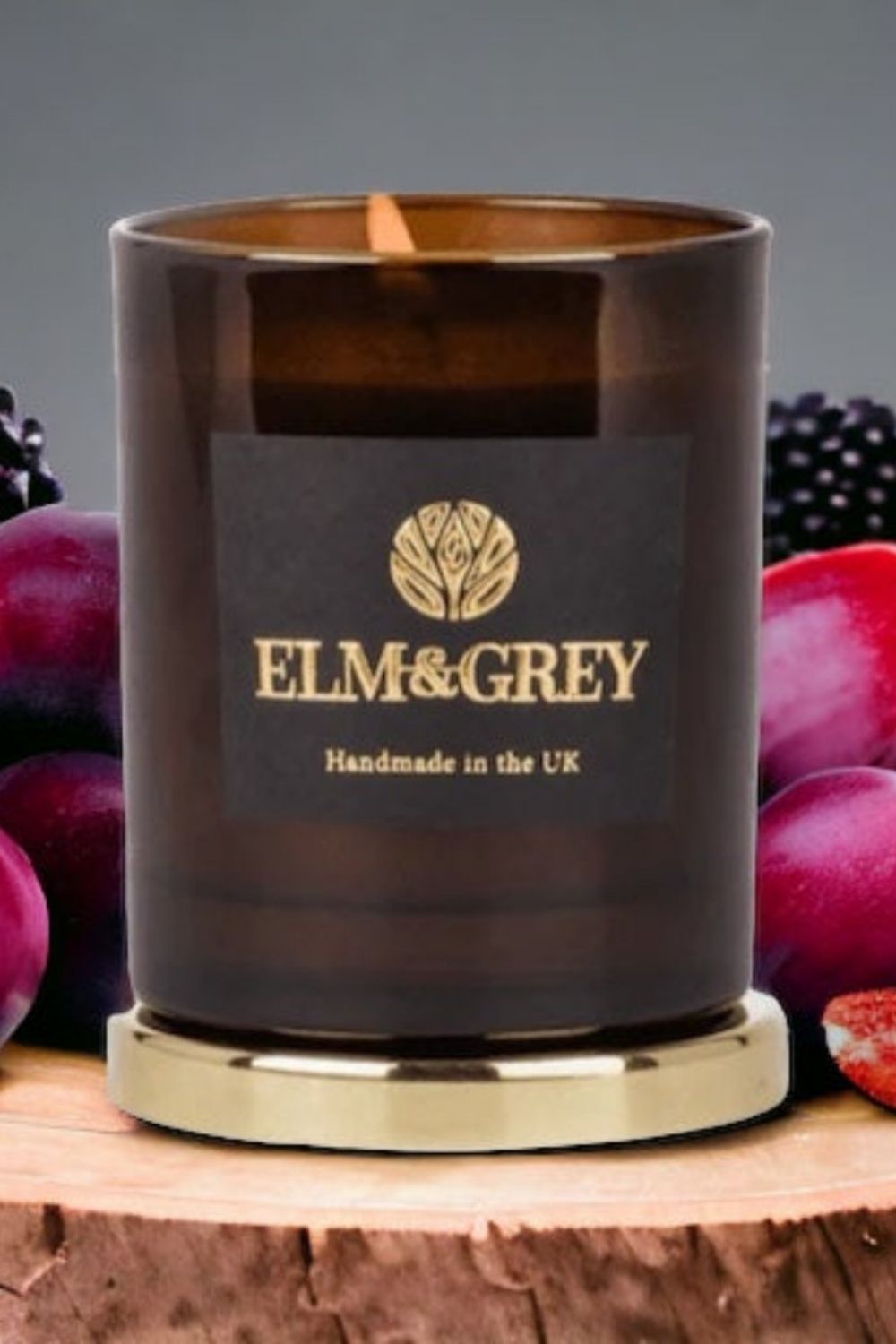 Candle with Elm & Grey branding surrounded by plums on a wooden surface