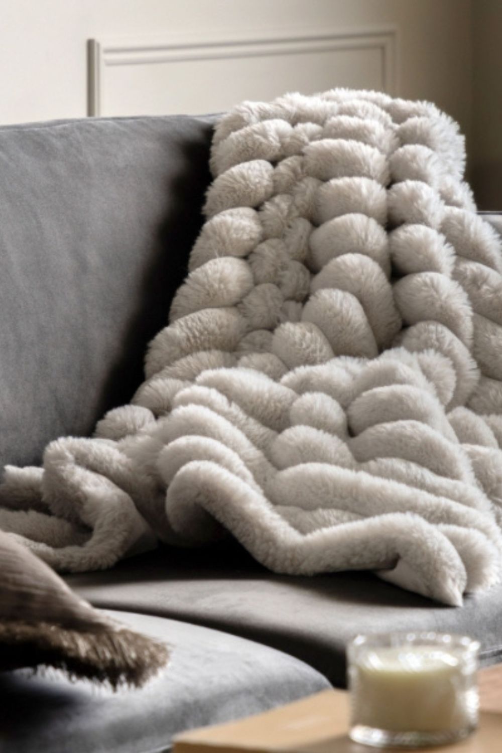 Textured beige blanket draped over a sofa with a candle and book in the foreground.