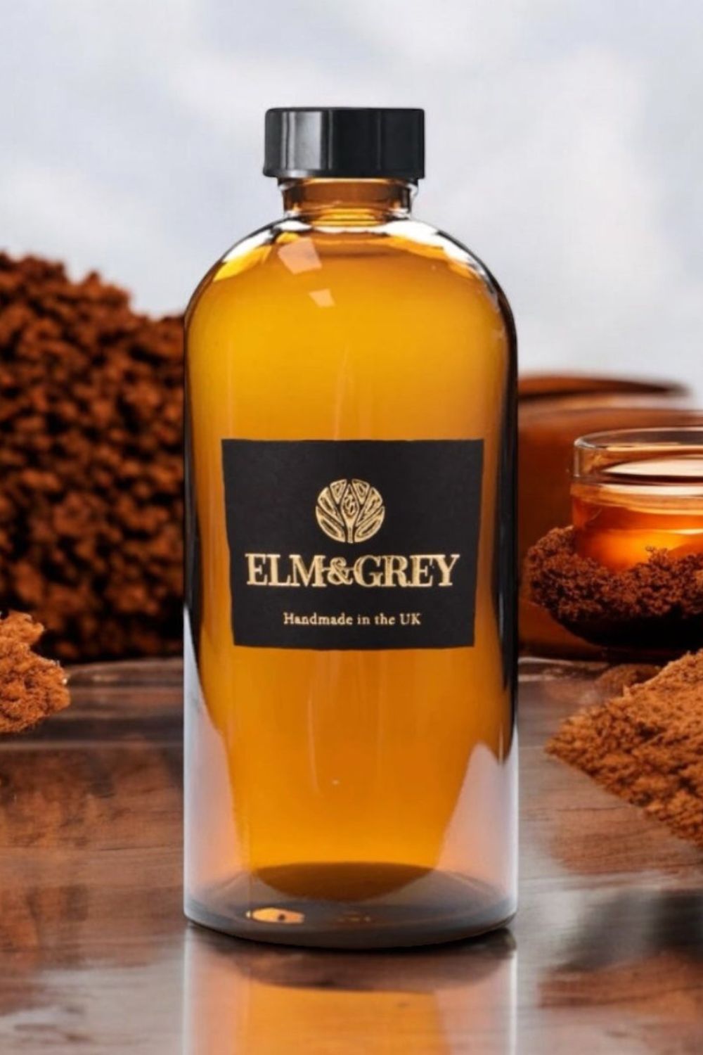 Bottle of Elm & Grey diffuser refill fluid on a reflective surface with blurred background