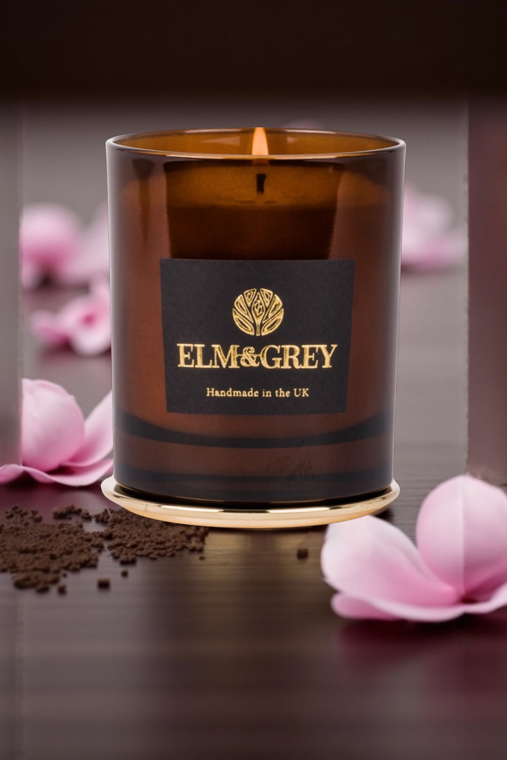 Brown candle with 'ELM & GREY' label on a dark surface with pink flowers.