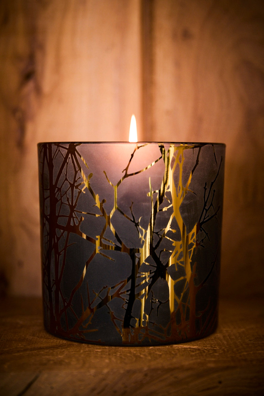 Candle in a decorative container with tree branch design on a wooden background