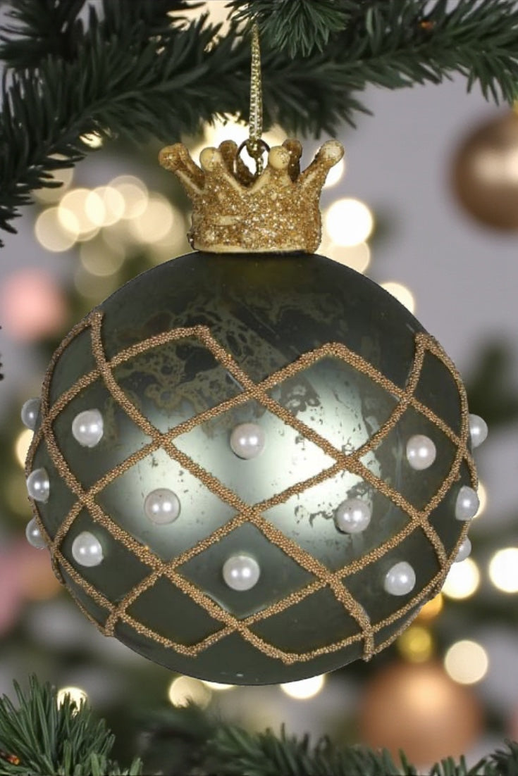 Decorative Christmas ornament with gold crown and pearl details on a tree.