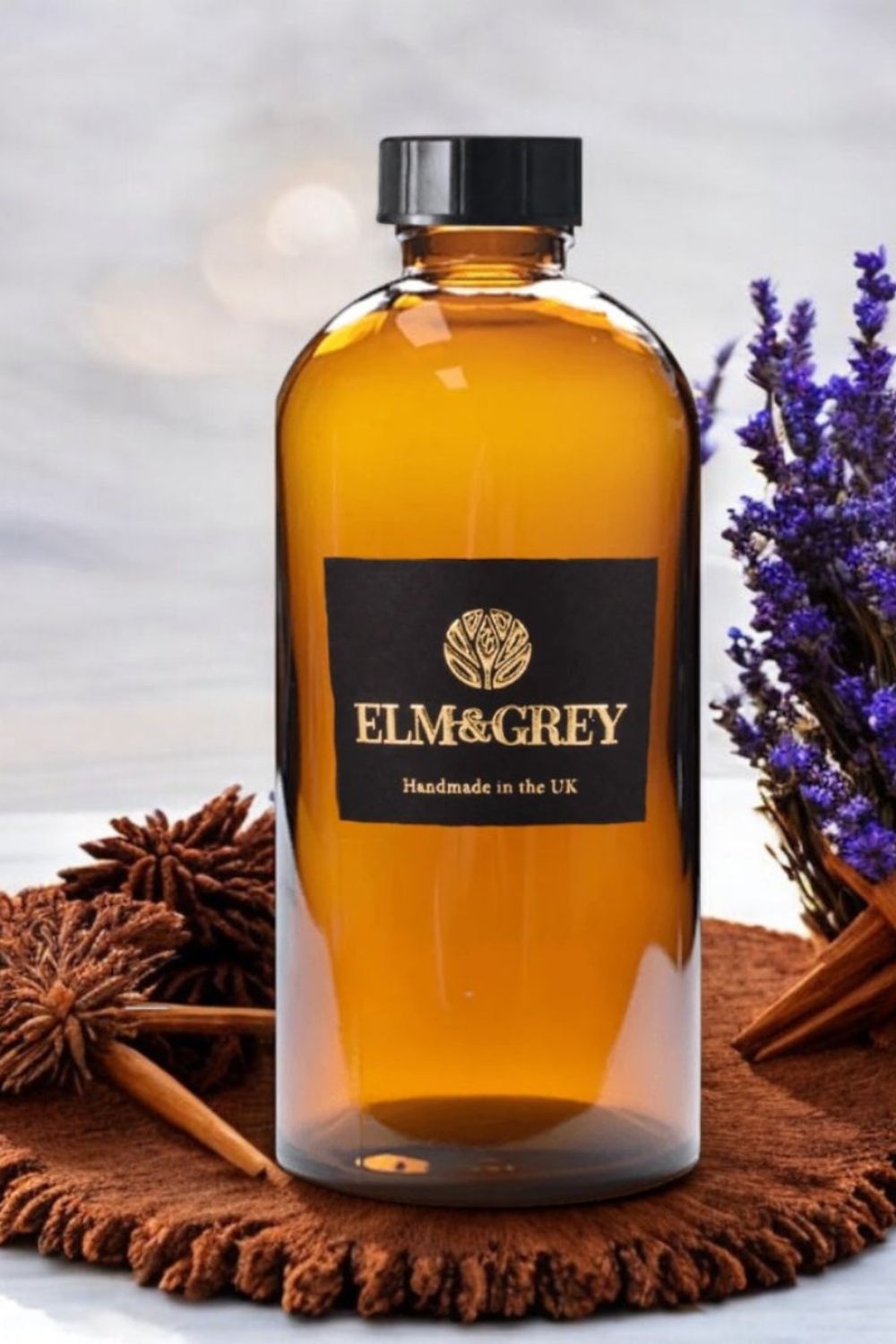 Bottle of Elm & Grey myrrh and tonka diffuser refill on a textured surface with lavender and cinnamon sticks.