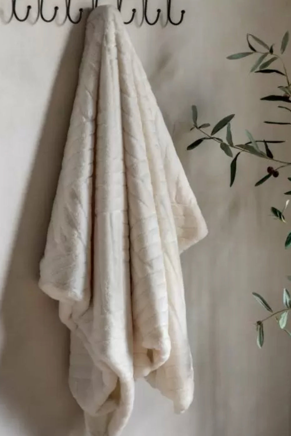 cream throw hanging on a hook against a light wall with a plant in the corner.