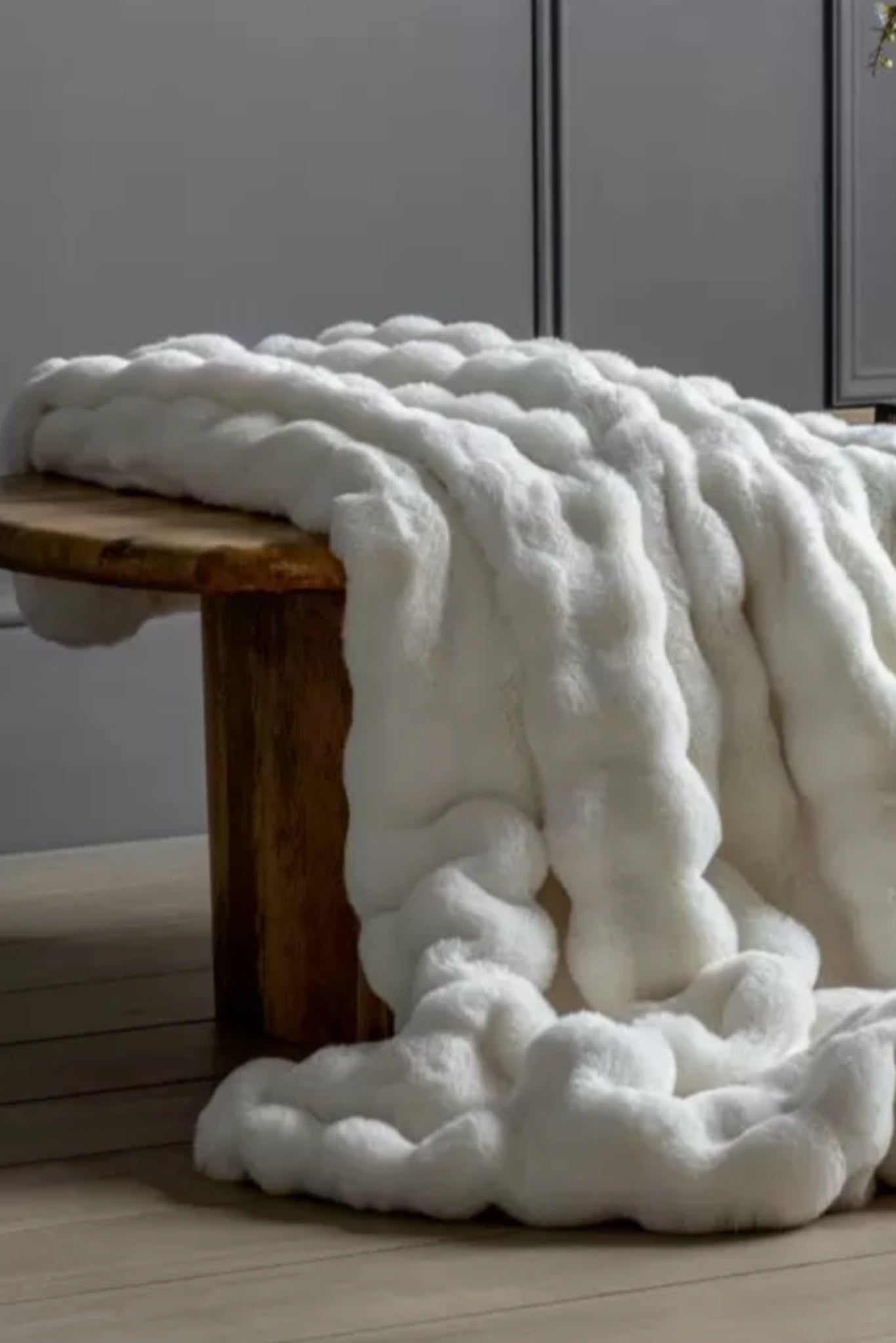 White blanket draped over a wooden stool against a gray wall.