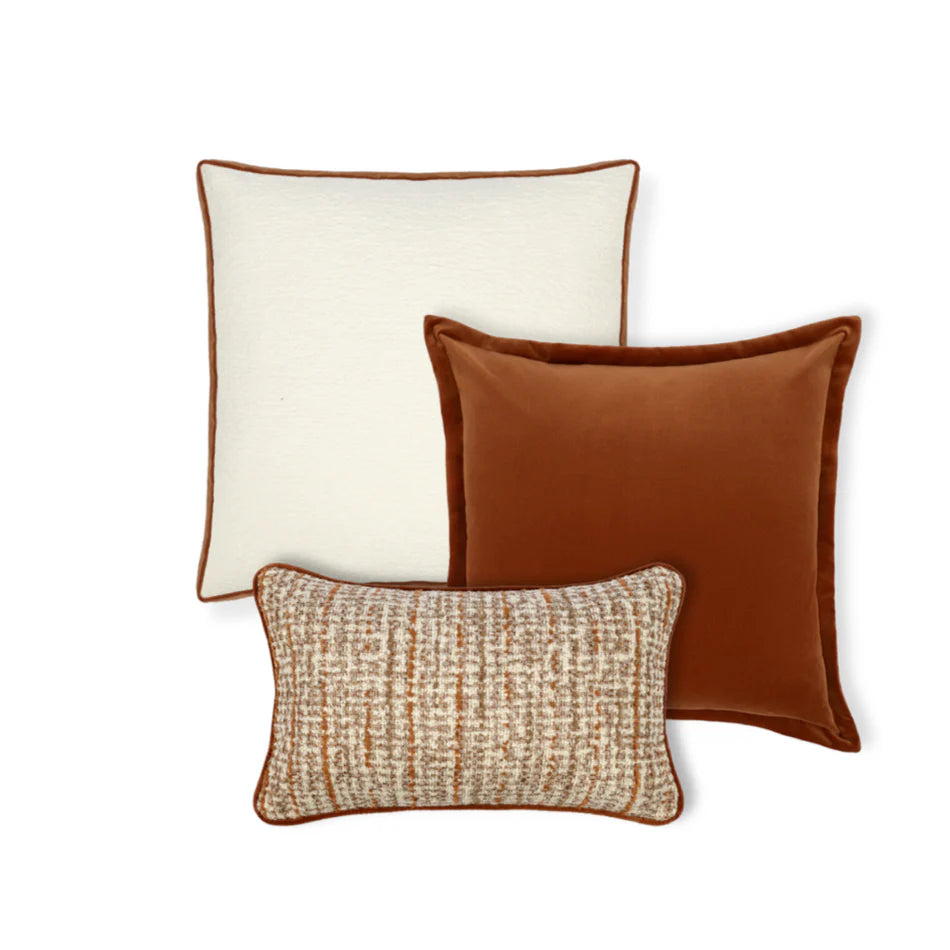 A trio of throw cushions with a cream cushion, an orange-brown velvet cushion, and a beige cushion with a woven texture.