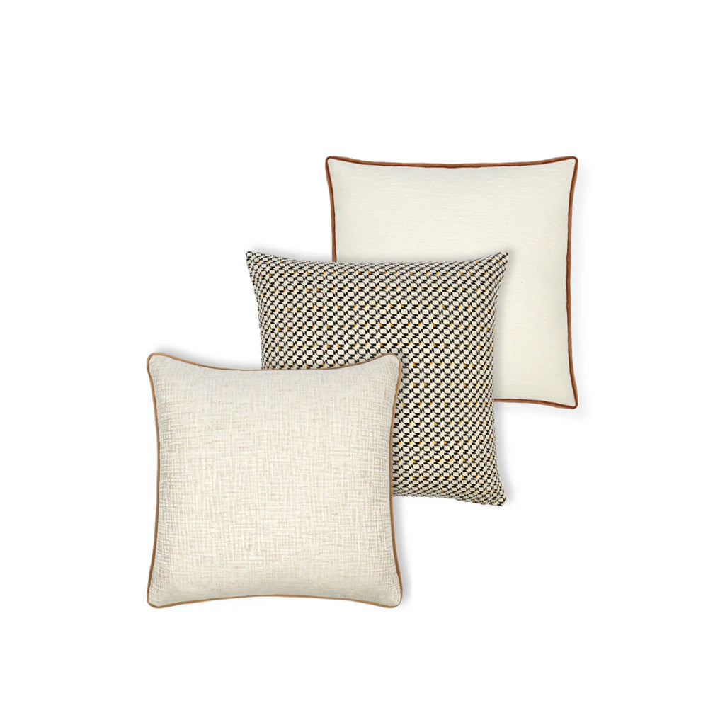 A set of three cushions, with the top cushion having a geometric onyx pattern, the middle cushion in a plain pearl color, and the bottom cushion in a bouclé texture with a contrast velvet band.