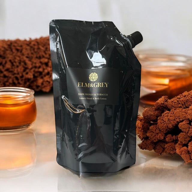 Elm & Grey Dark Honey & Tobacco Luxury Hand & Body Lotion 450ml Black Refill Pouch sitting on a surface with honey and spices in the background