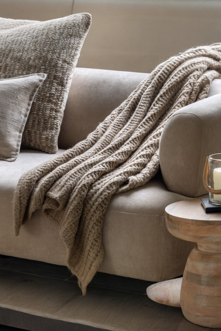 Beige sofa with a textured blanket and pillow, wooden side table with candle