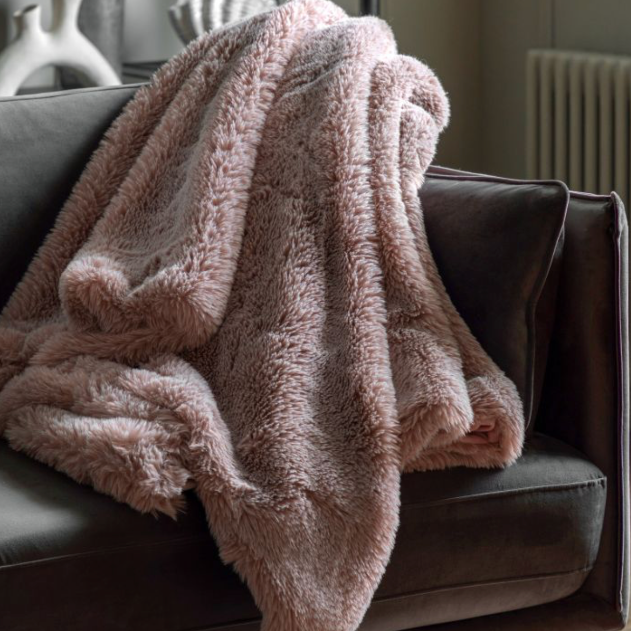 A dusty mauve pink heavyweight faux fur throw draped over a dark-colored armchair in a cozy living room setting.