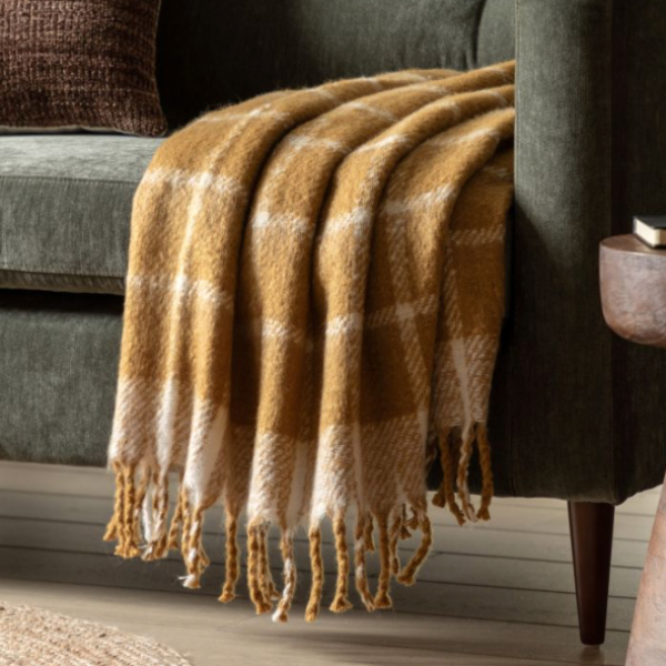A mustard yellow and white checkered throw blanket draped over a couch, with fringing detail on the edges.
