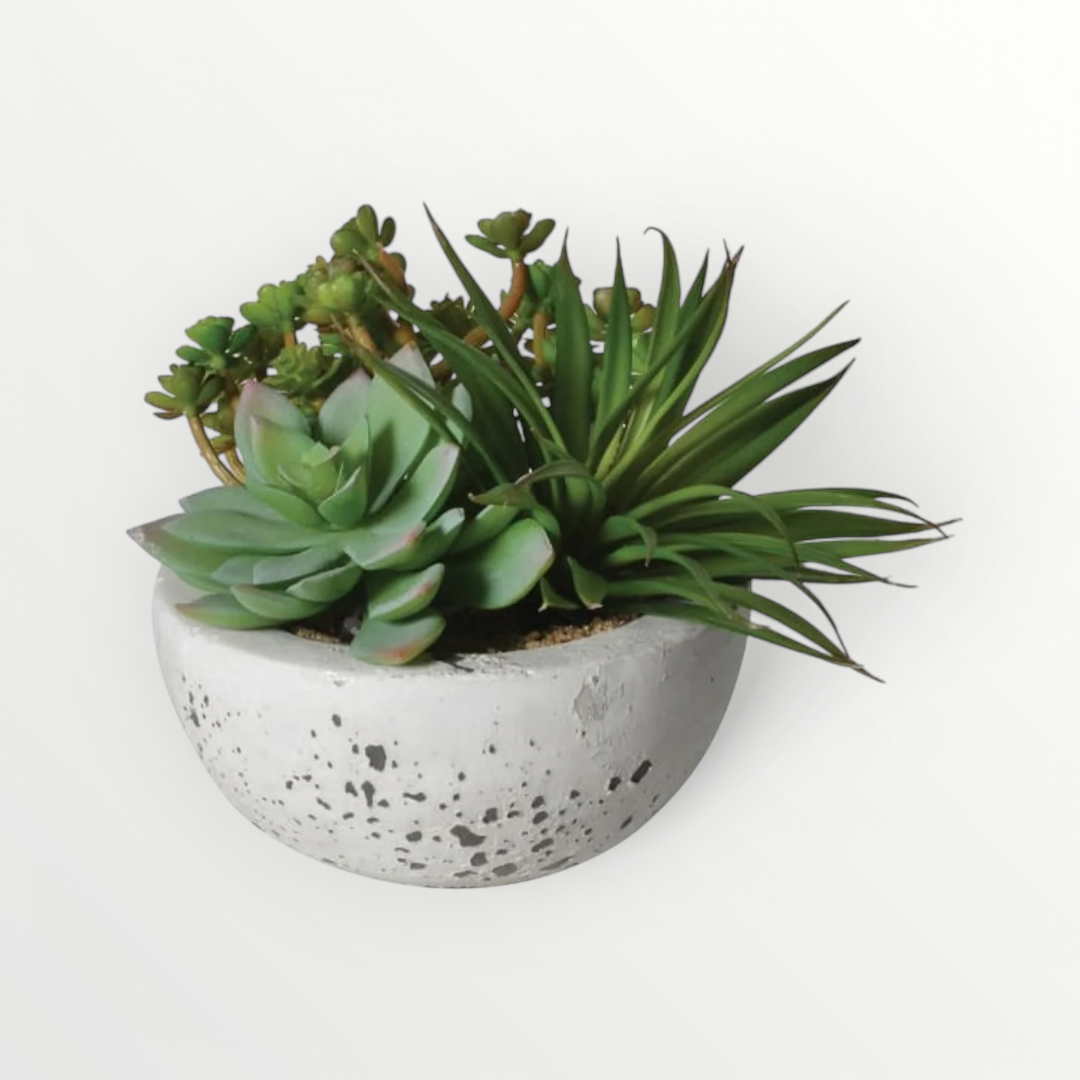 Assorted faux green succulents arranged inside a grey cement bowl.