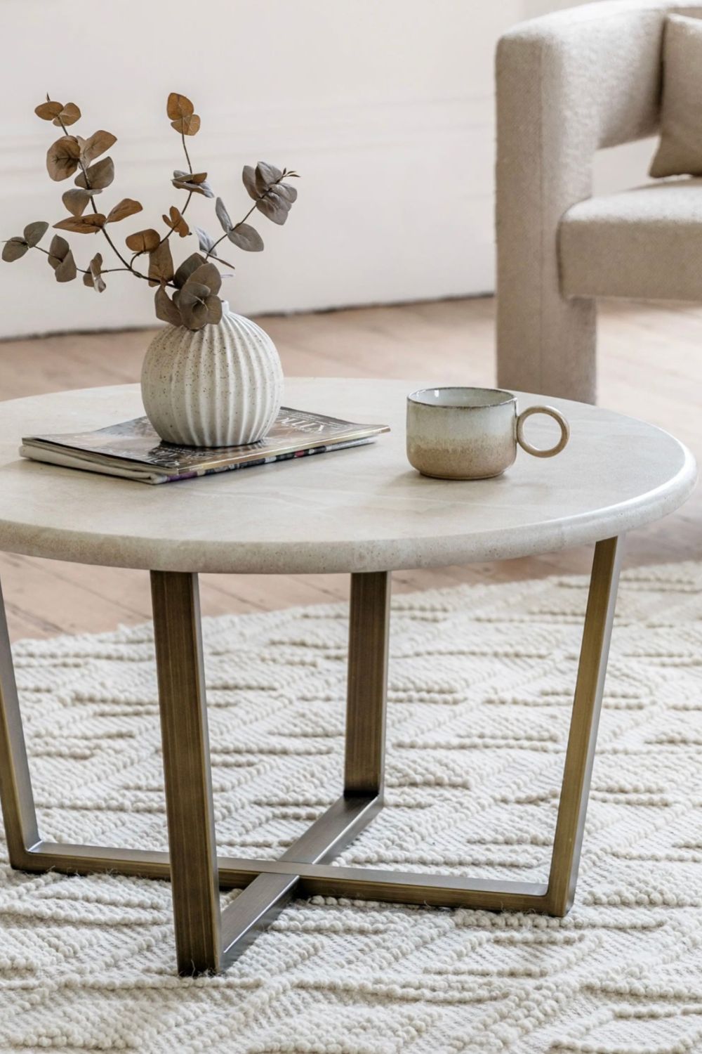 Round travertine effect coffee table with decorative items in a living room setting