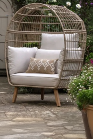 Wicker egg-shaped chair with beige cushions and a patterned pillow on a stone patio.