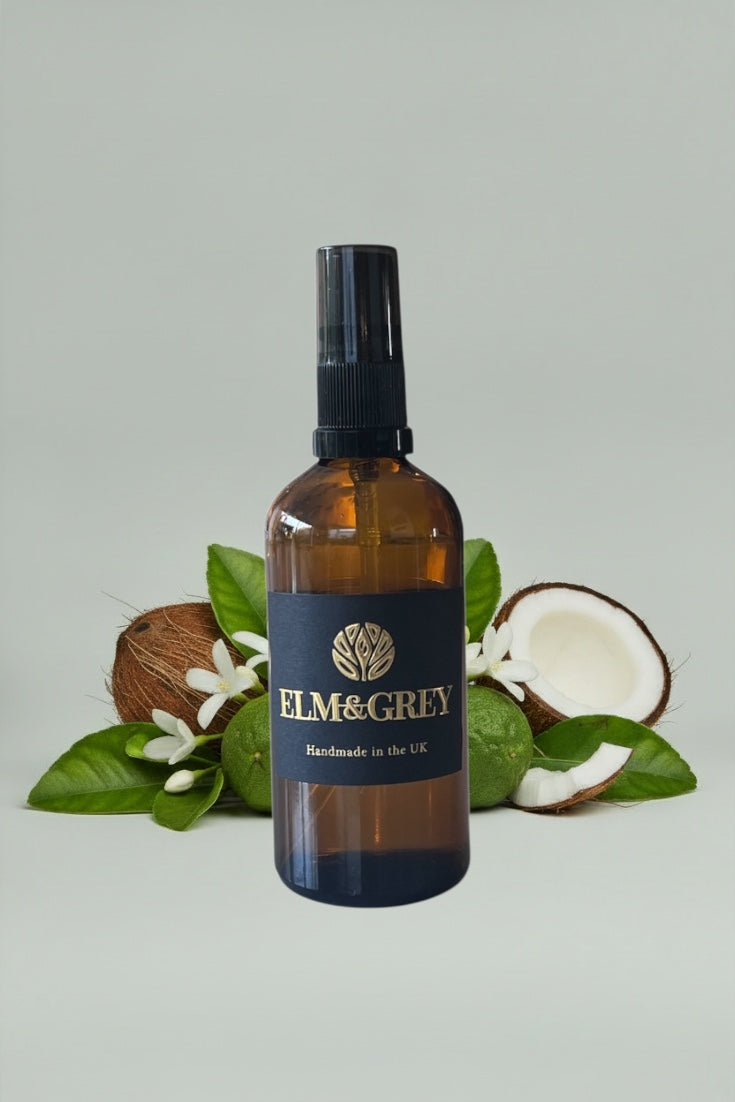 Amber glass bottle with black cap labeled 'Elm & Grey' on a light grey background with coconuts and leaves.