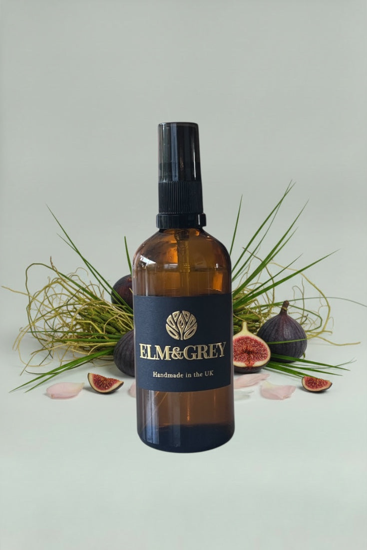 Brown bottle with black cap labeled 'Elm & Grey' on a light green background with figs and grass.