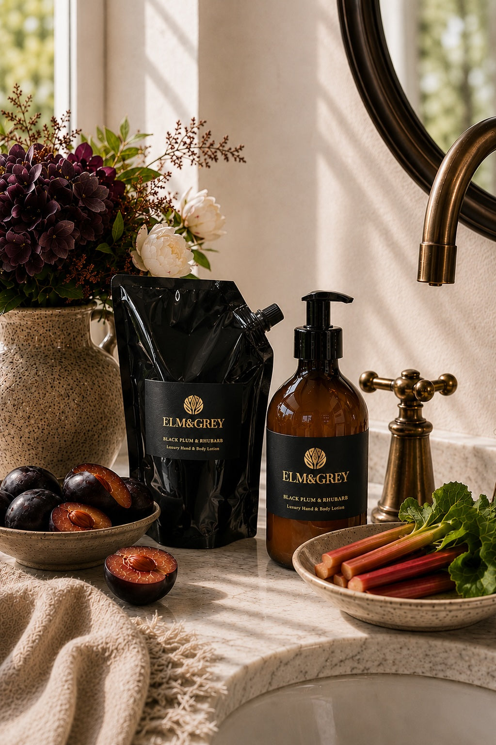 Black plum and rhubarb hand and body lotion bottle and refill pouch on a marble bathroom countertop with flowers and fruit