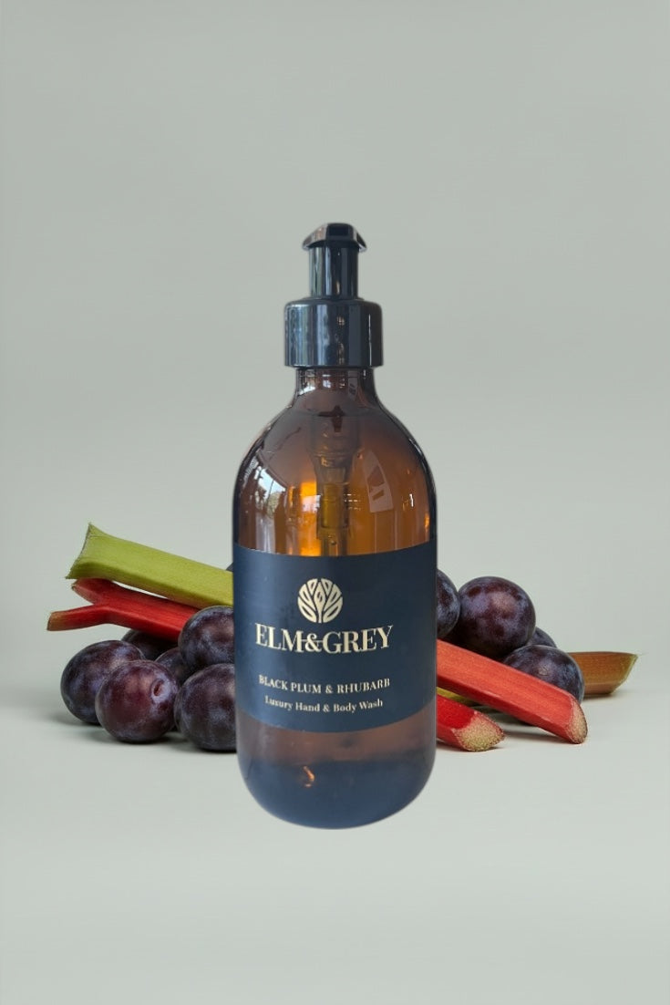 Amber bottle of Elm & Grey Black Plum & Rhubarb product with plums and rhubarb stalks on a light gray background
