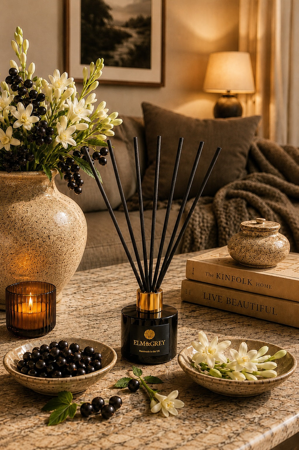 Blackcurrant and tuberose reed diffuser styled on a marble coffee table in a luxurious living room with flowers and a lit candle