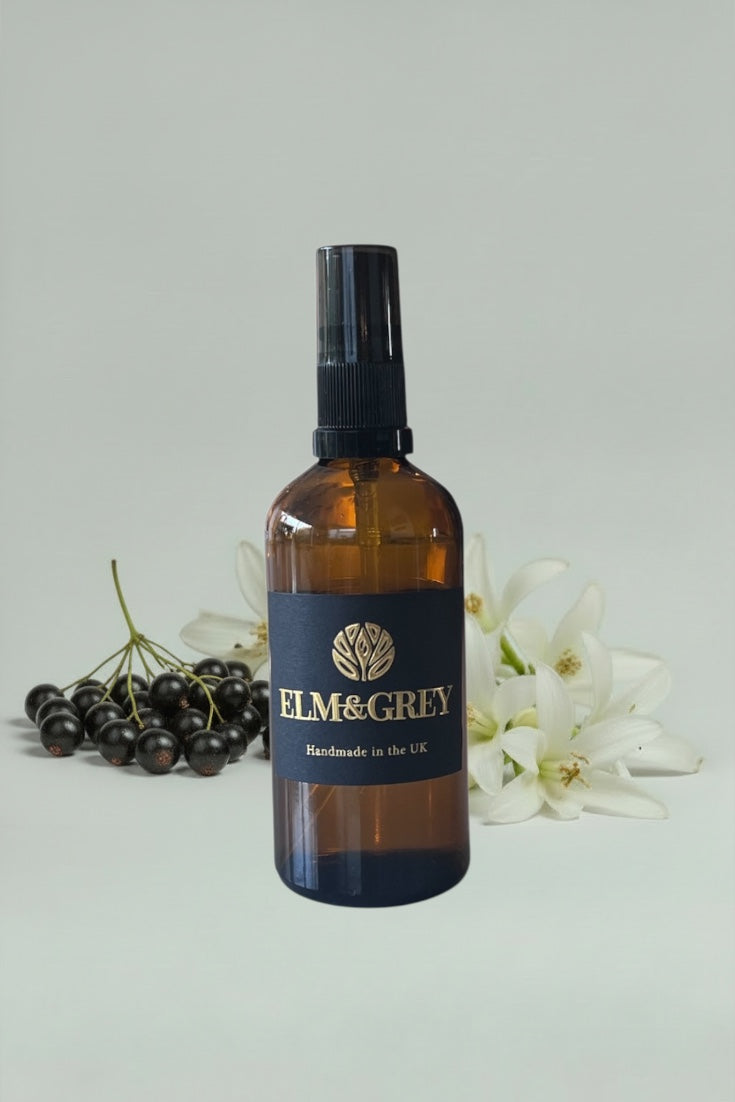 Brown bottle with black cap labeled 'Elm & Grey' on a light gray background with berries and flowers.