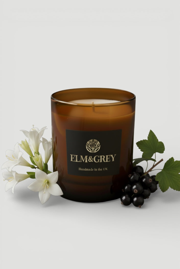 blackcurrant and tuberose candle with 'Elm & Grey' label surrounded by flowers and leaves on a light background