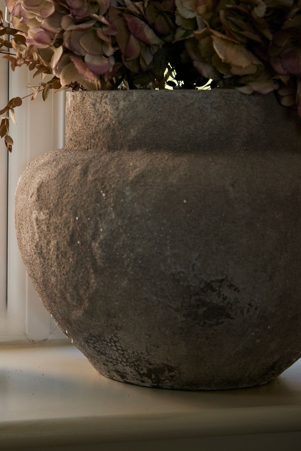 Decorative stone vase with dried flowers on a windowsill