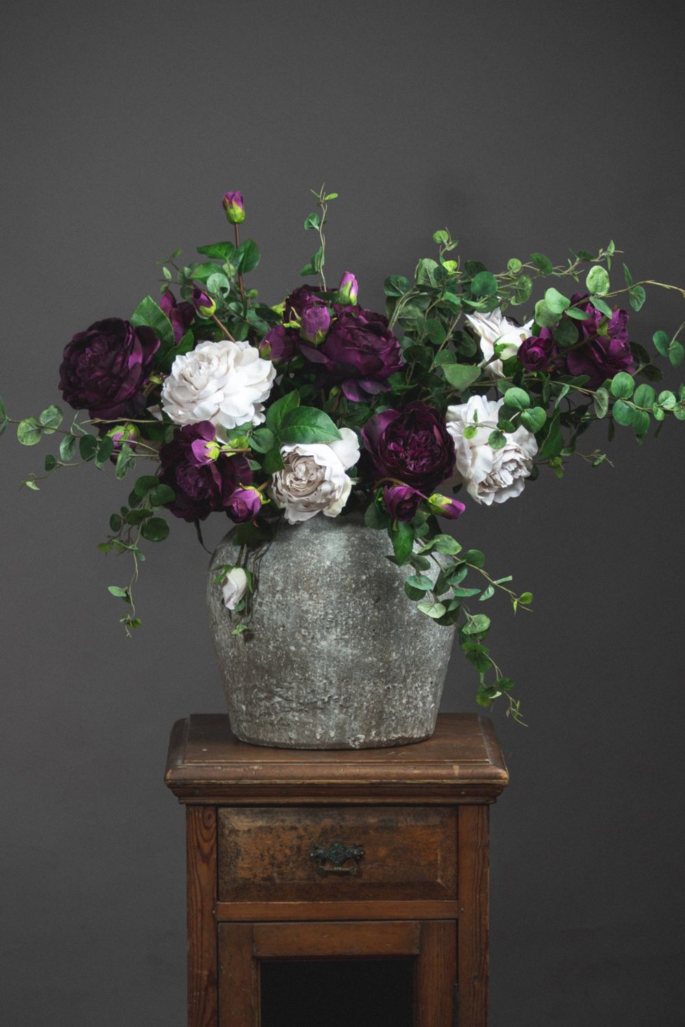 Bouquet of purple and white flowers in a textured vase on a wooden table against a gray background