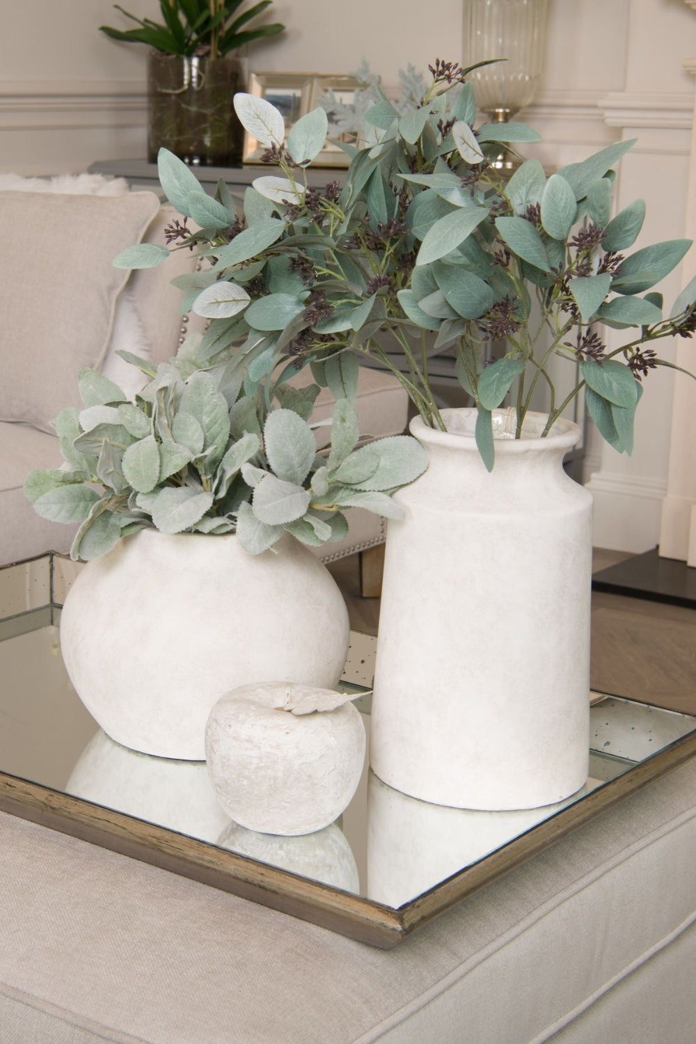 Decorative arrangement of white vases with greenery on a reflective surface.