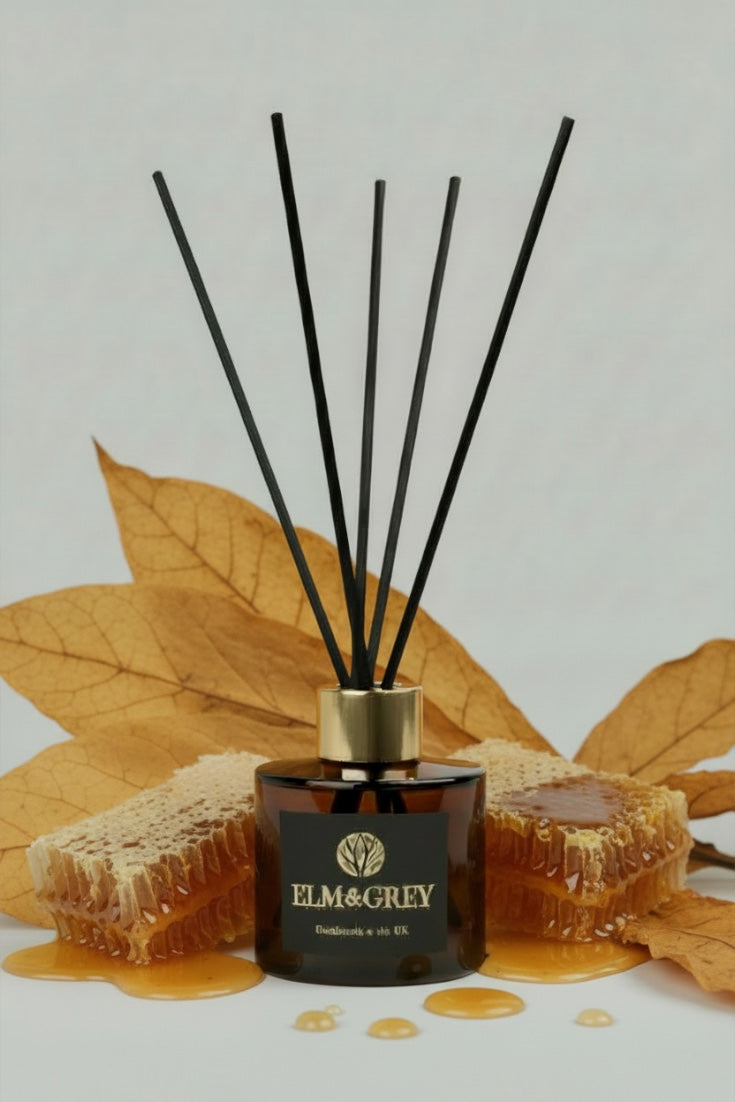 Reed diffuser with black sticks and gold cap on a white background with honeycomb and honey.