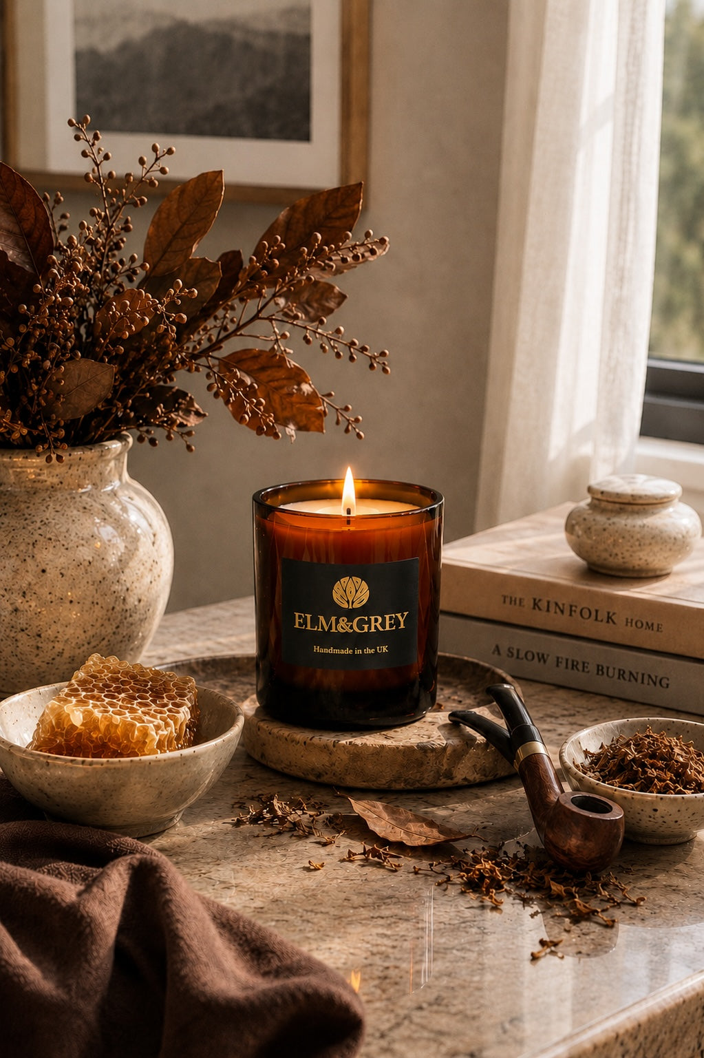 Dark honey and tobacco scented candle by elm and grey styled on a marble surface with books, flowers and botanicals
