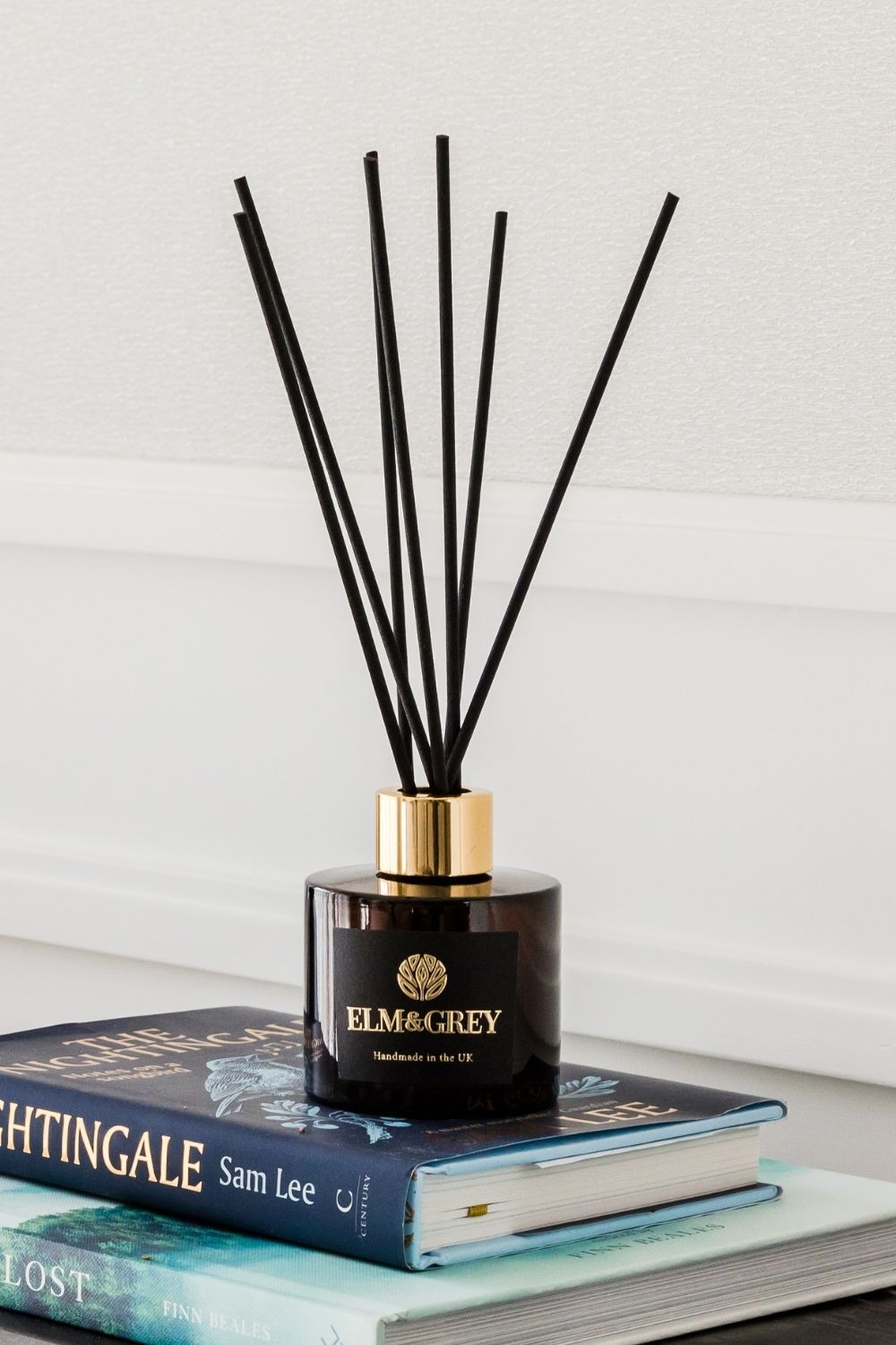 Reed diffuser with black sticks on a stack of books against a light background