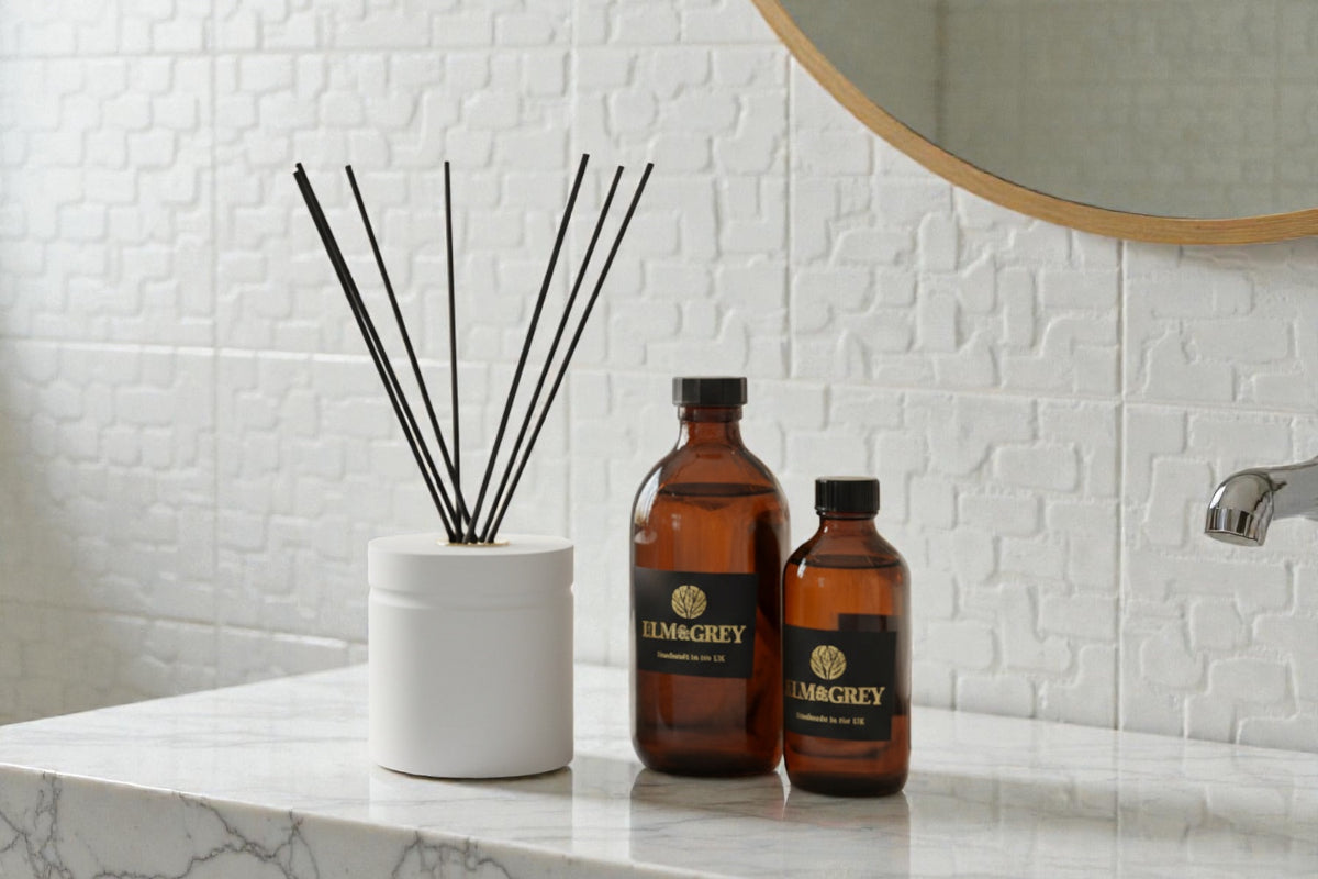 Two amber bottles labeled Elm and Grey on a bathroom counter with a diffuser in the background.