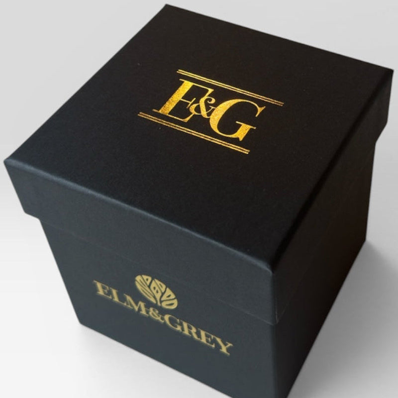 Elm & Grey matte black gift box with gold E&G monogram foil on lid and gold Elm & Grey logo on side, product shot on grey background