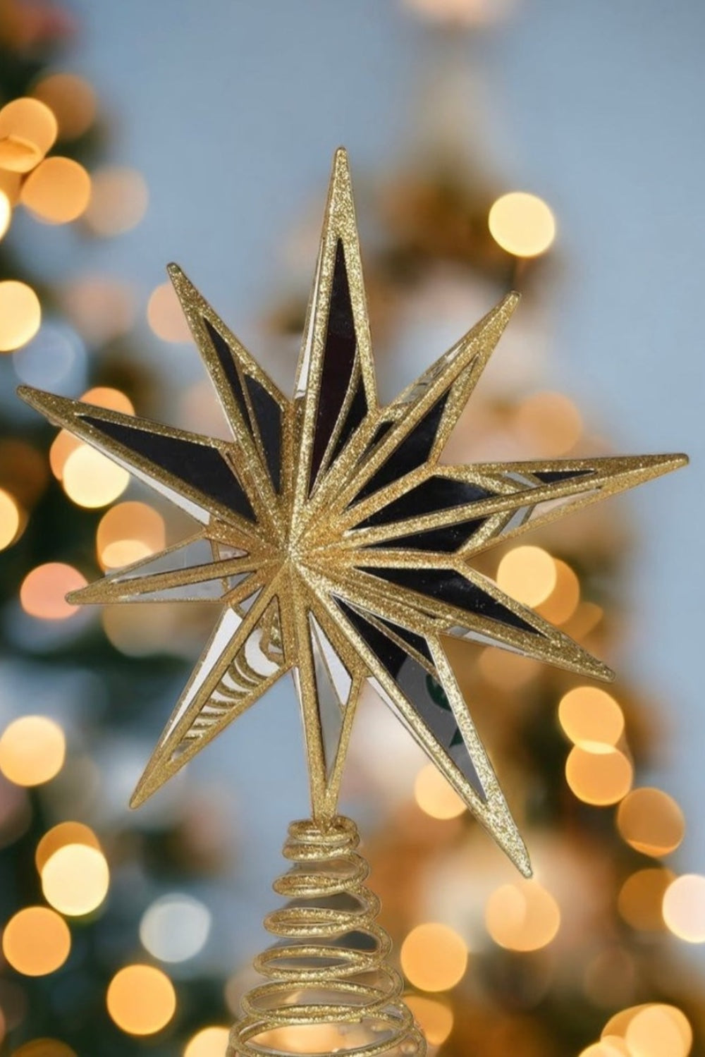 Decorative gold star tree topper against a blurred Christmas tree background with lights.