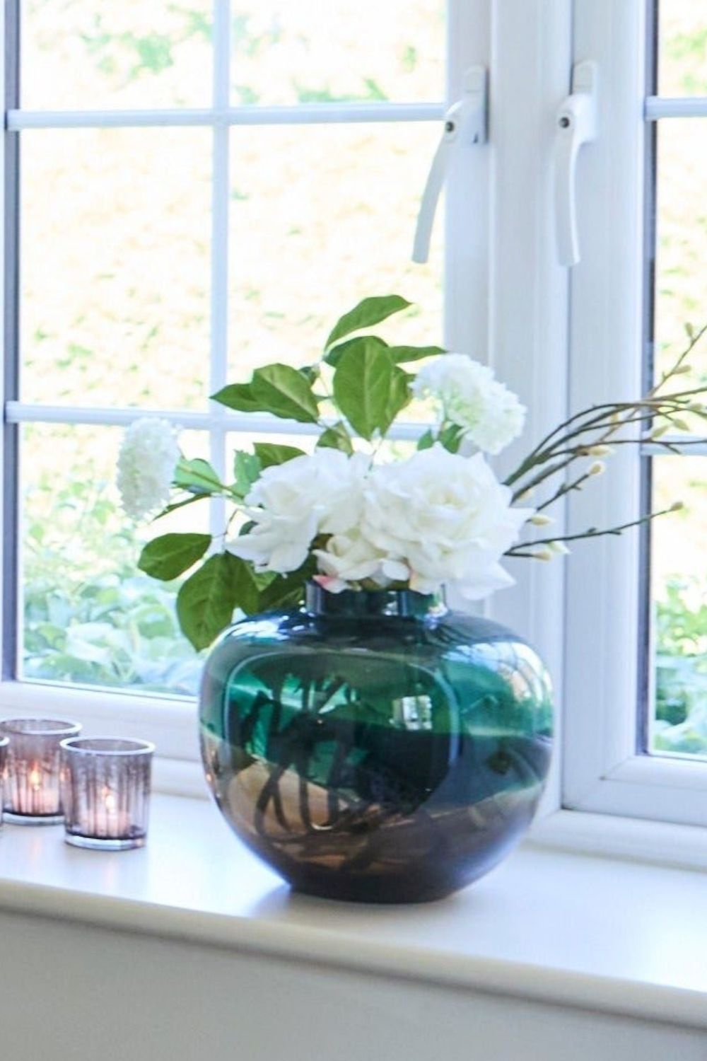 Green vase with white flowers on a windowsill with light background