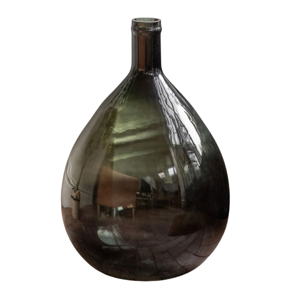 A large teardrop-shaped glass vase with a narrow neck, made of dark smoky green glass that reflects the surrounding room.
