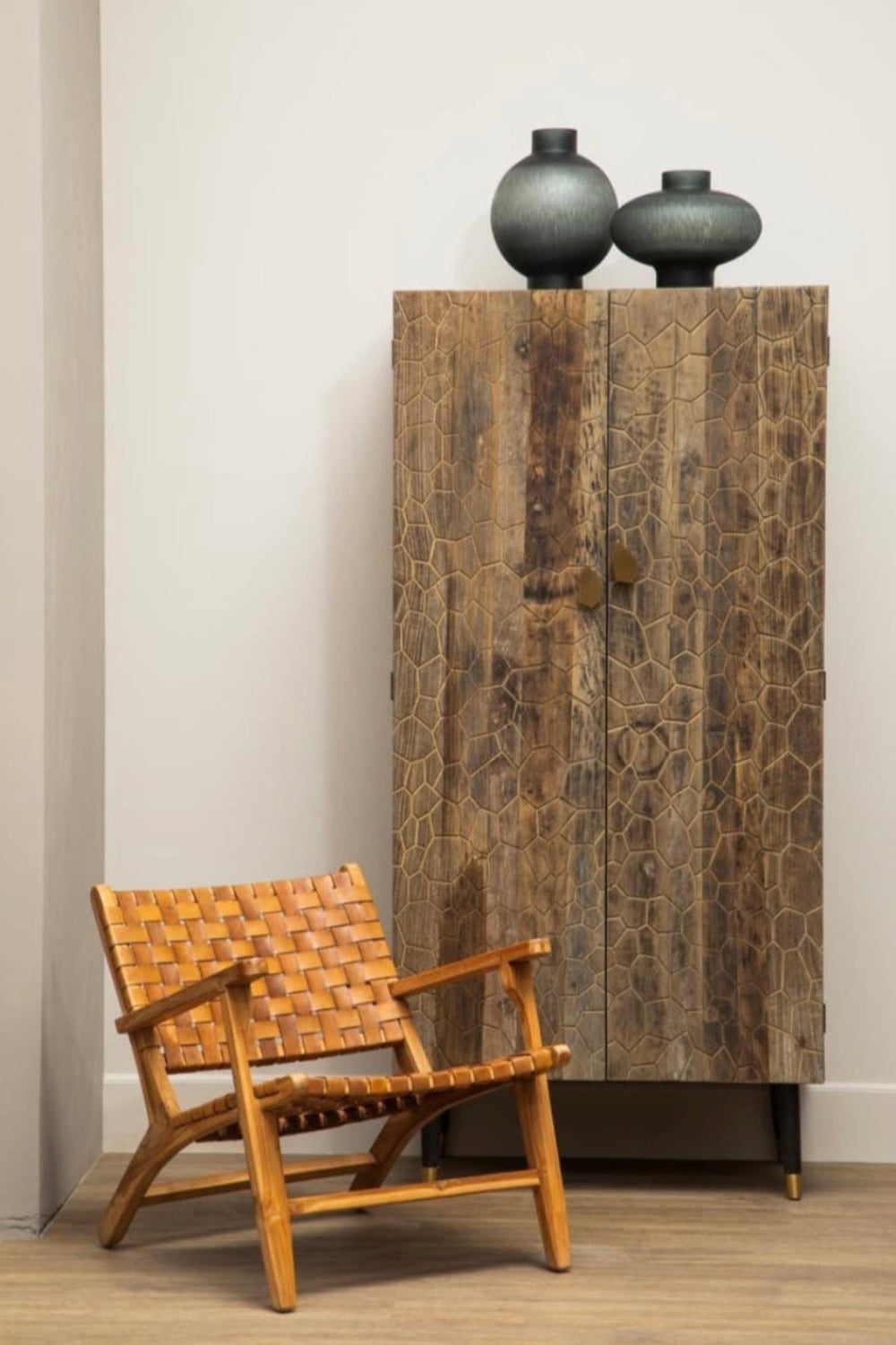 Wooden armchair next to a tall wooden cabinet with two grey cut glass vases on top.