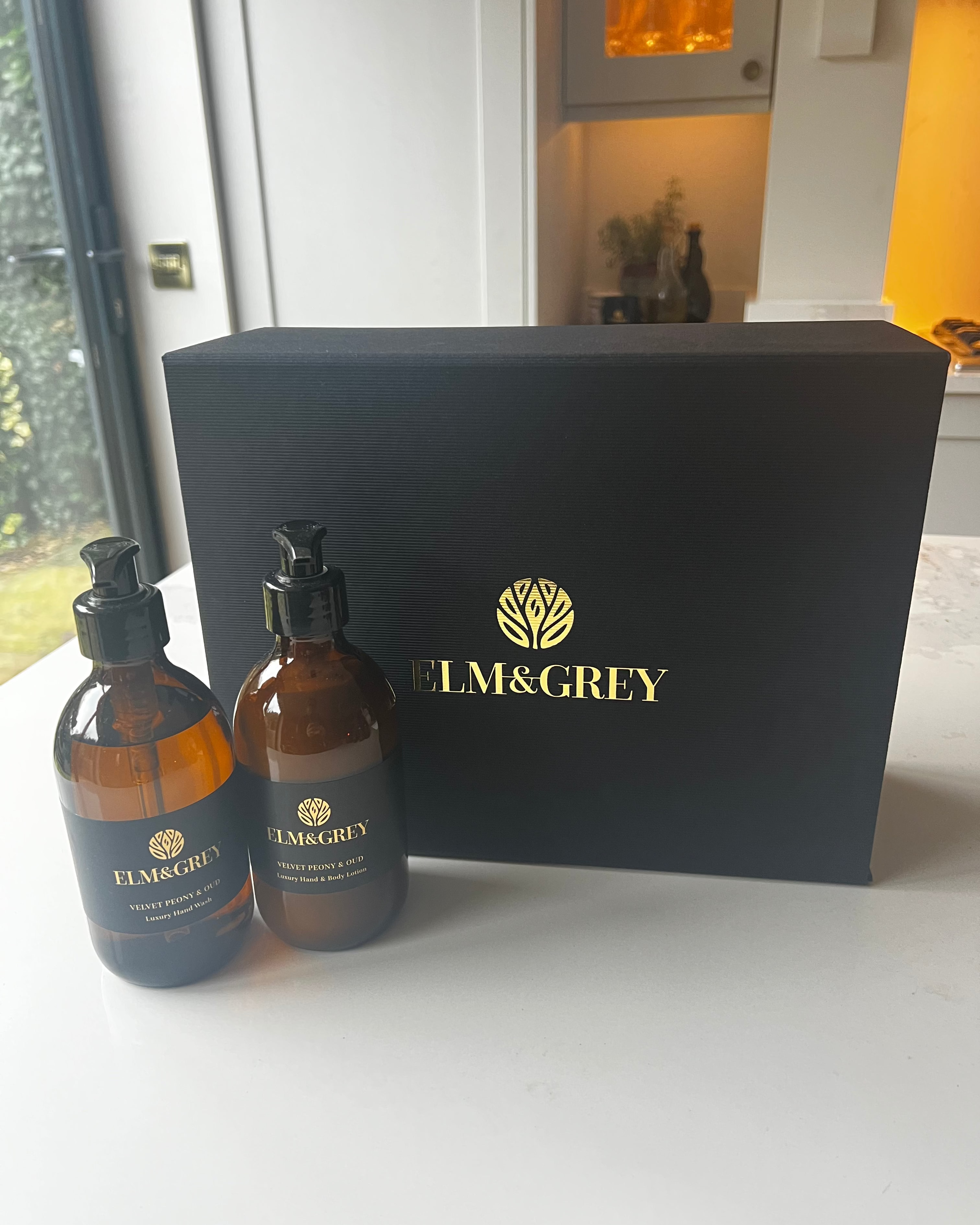 Two bottles of Elm & Grey products in front of a black box with the brand logo.