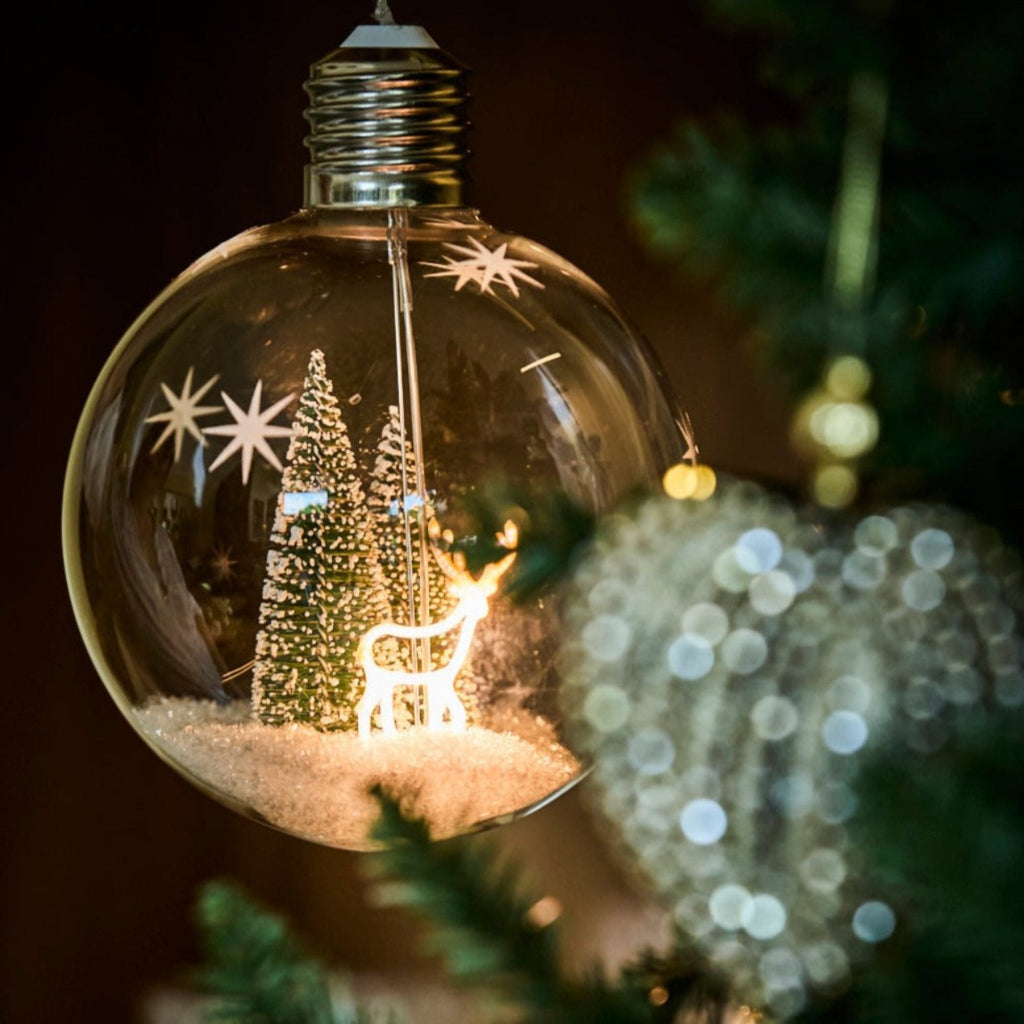 Decorative light bulb with Christmas scene inside, surrounded by festive lights.