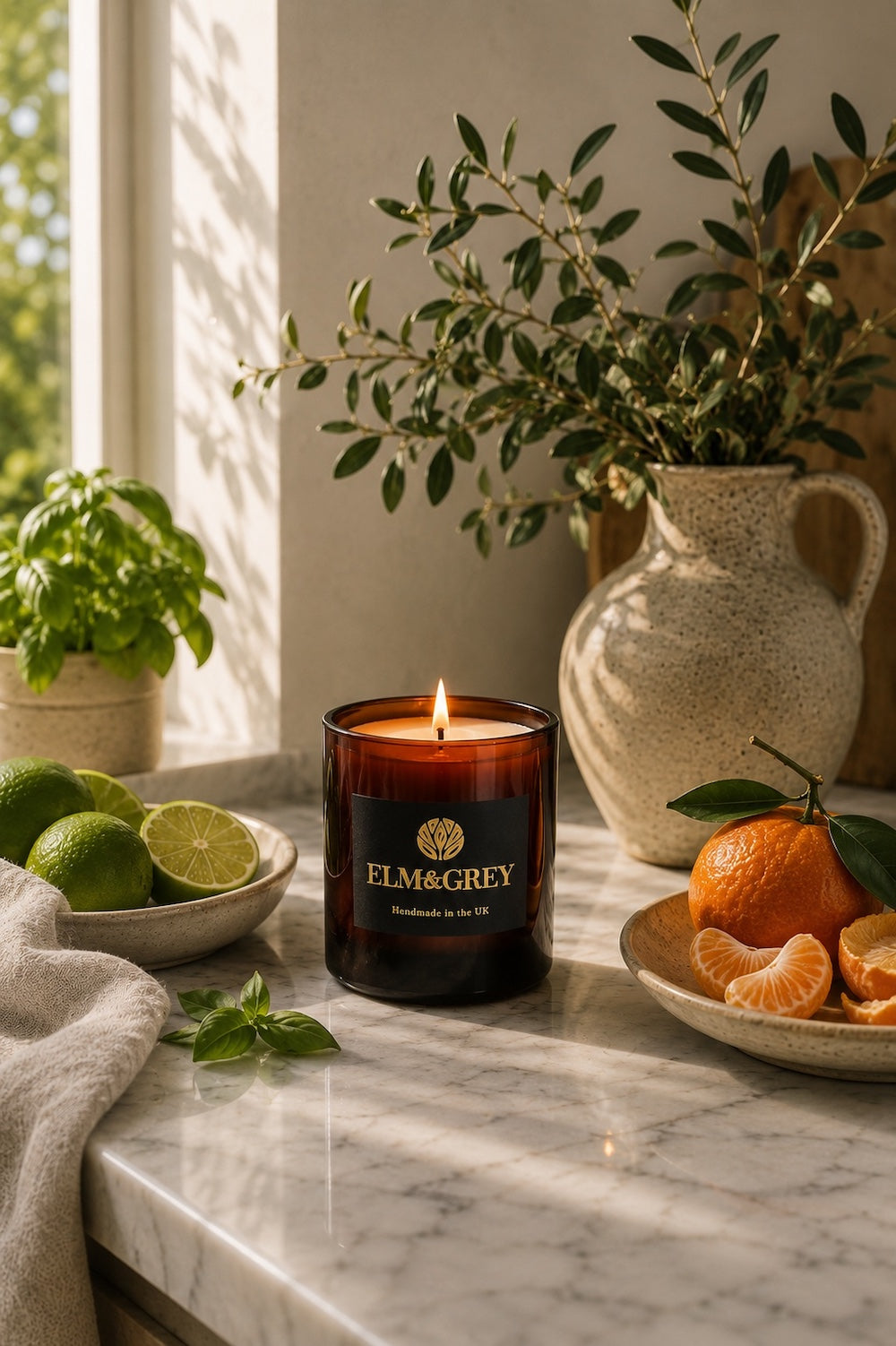 Elm & Grey Lime Basil & Mandarin luxury candle styled on a marble bathroom countertop with fresh limes, basil and mandarin