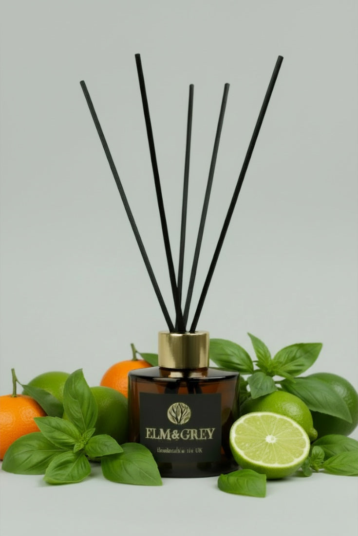 Diffuser with black sticks surrounded by green leaves and oranges on a light grey background