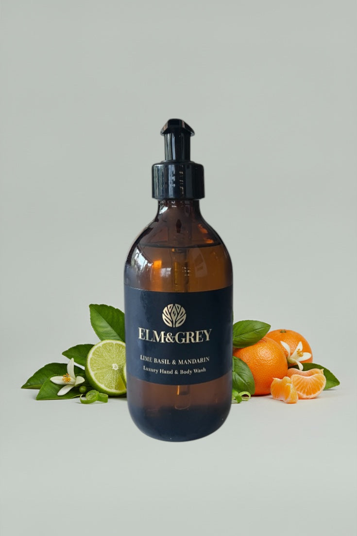 Amber bottle with black cap labeled 'Elm & Grey' on a light grey background with green leaves and oranges.