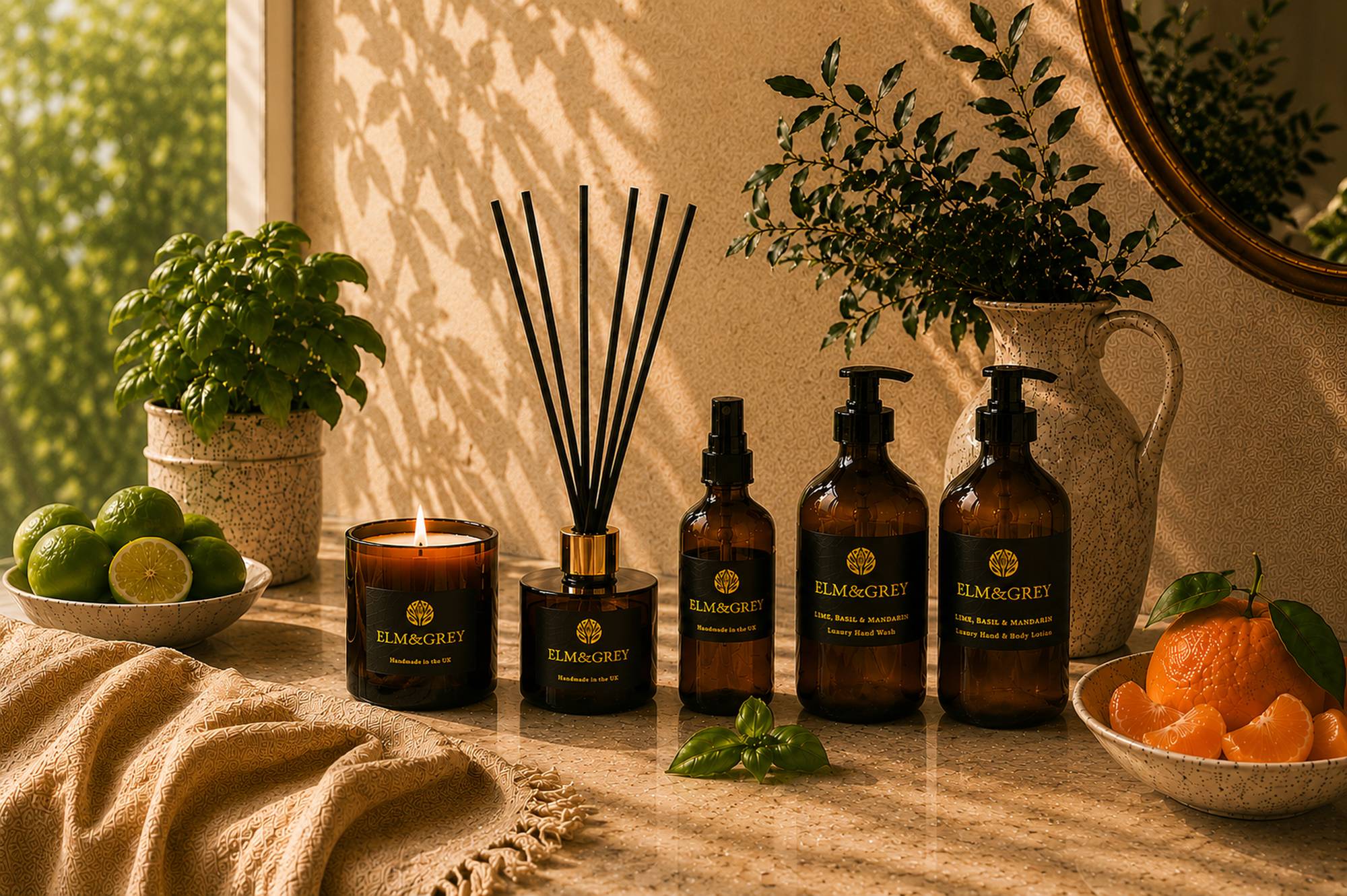 Collection of Elm and Grey products including room spray bottle, a lit candle, and reed diffuser on a wooden surface with plants and citrus fruit.