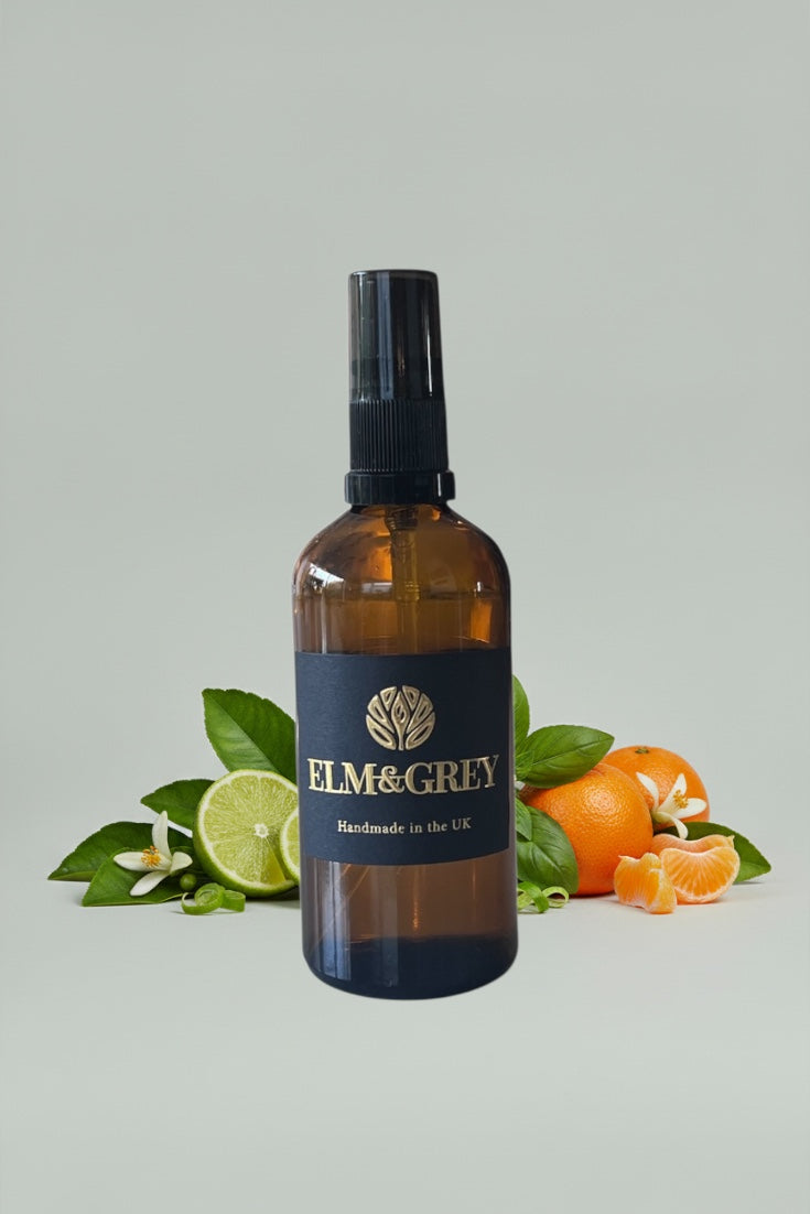 Bottle of Elm & Grey product with lime and orange slices on a light grey background