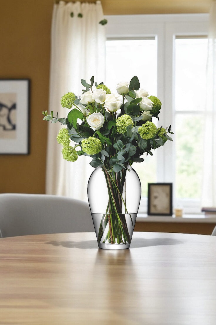 Vase with flowers on a table in a room with a window and framed picture.