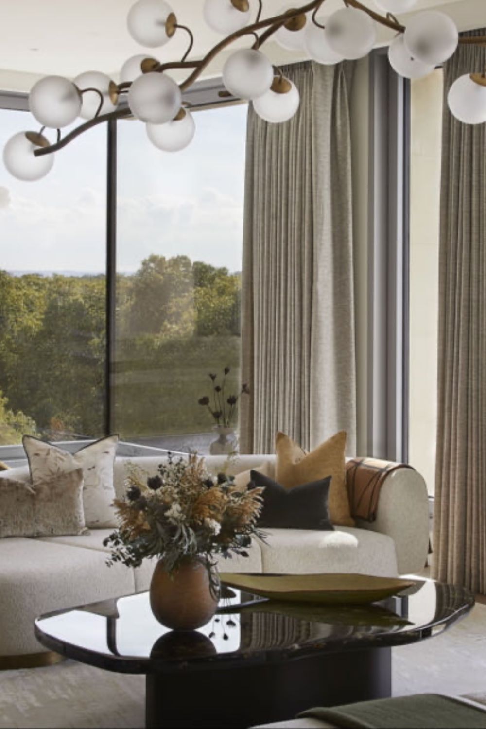 Modern living room with a sofa, coffee table, and large windows with an LSA brown boulder vase with dried flowers in the foreground.