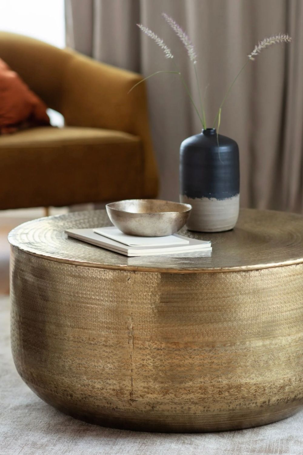 Round antique brass embossed coffee table with decorative items in a living room setting