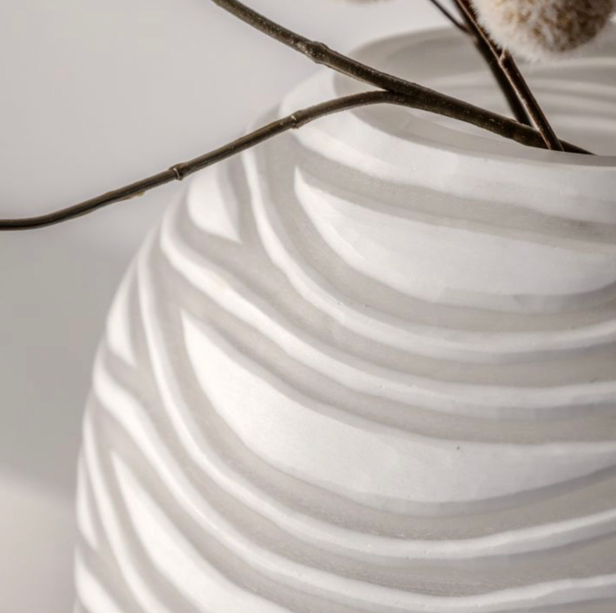White ceramic vase with wavy texture holding dried branches on a light background