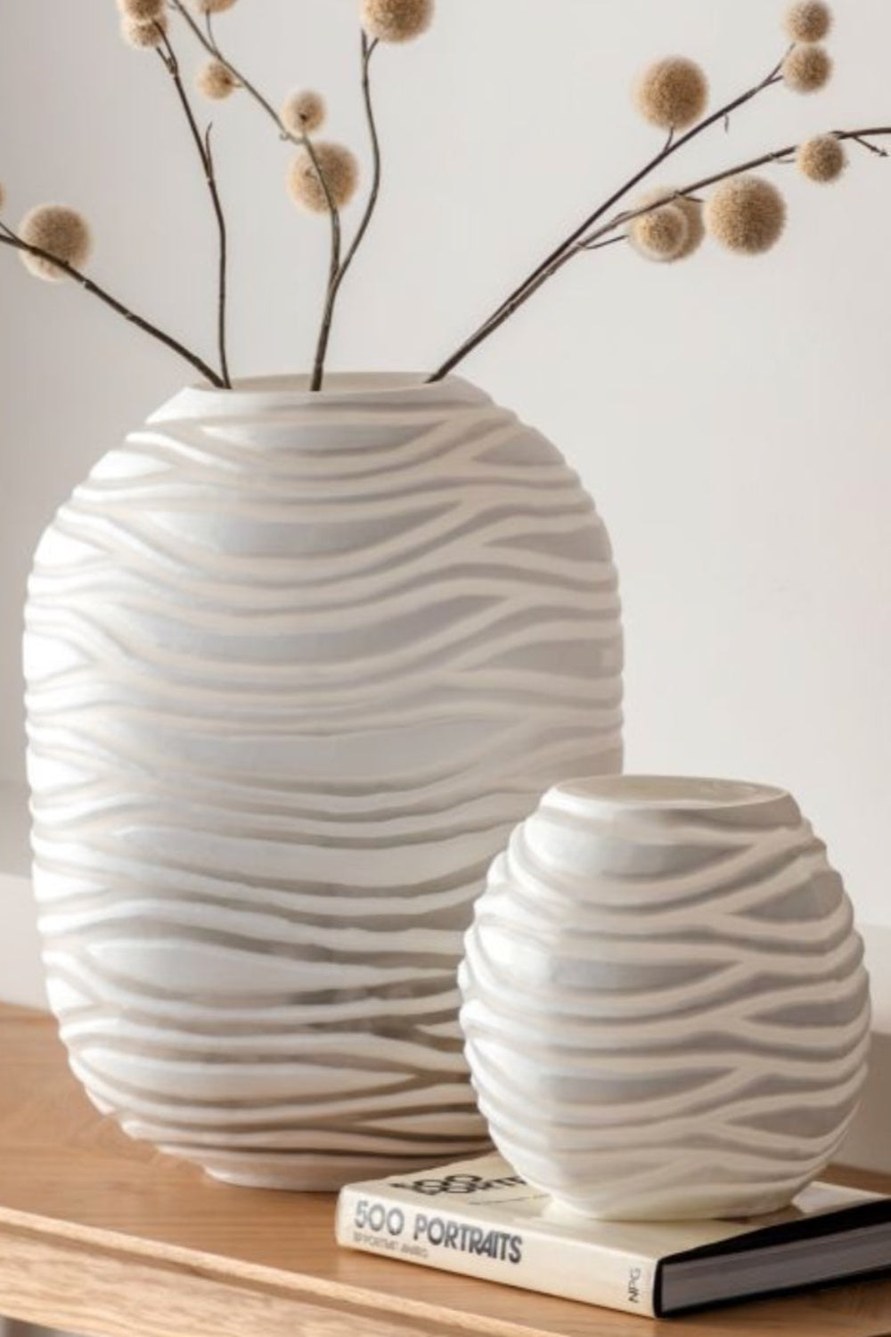White textured luna strata striped vases on a wooden surface with a book underneath.